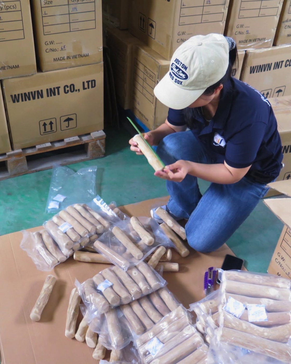 Worker individually poly-bagging coffee wood chews next to WINVN export cartons